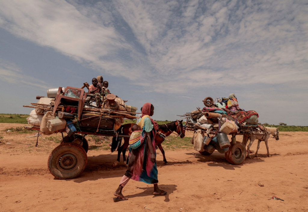 FILE PHOTO: A Sudanese woman, who fled the conflict in Murnei in Sudan's Darfur region, walks beside carts carrying her fa...